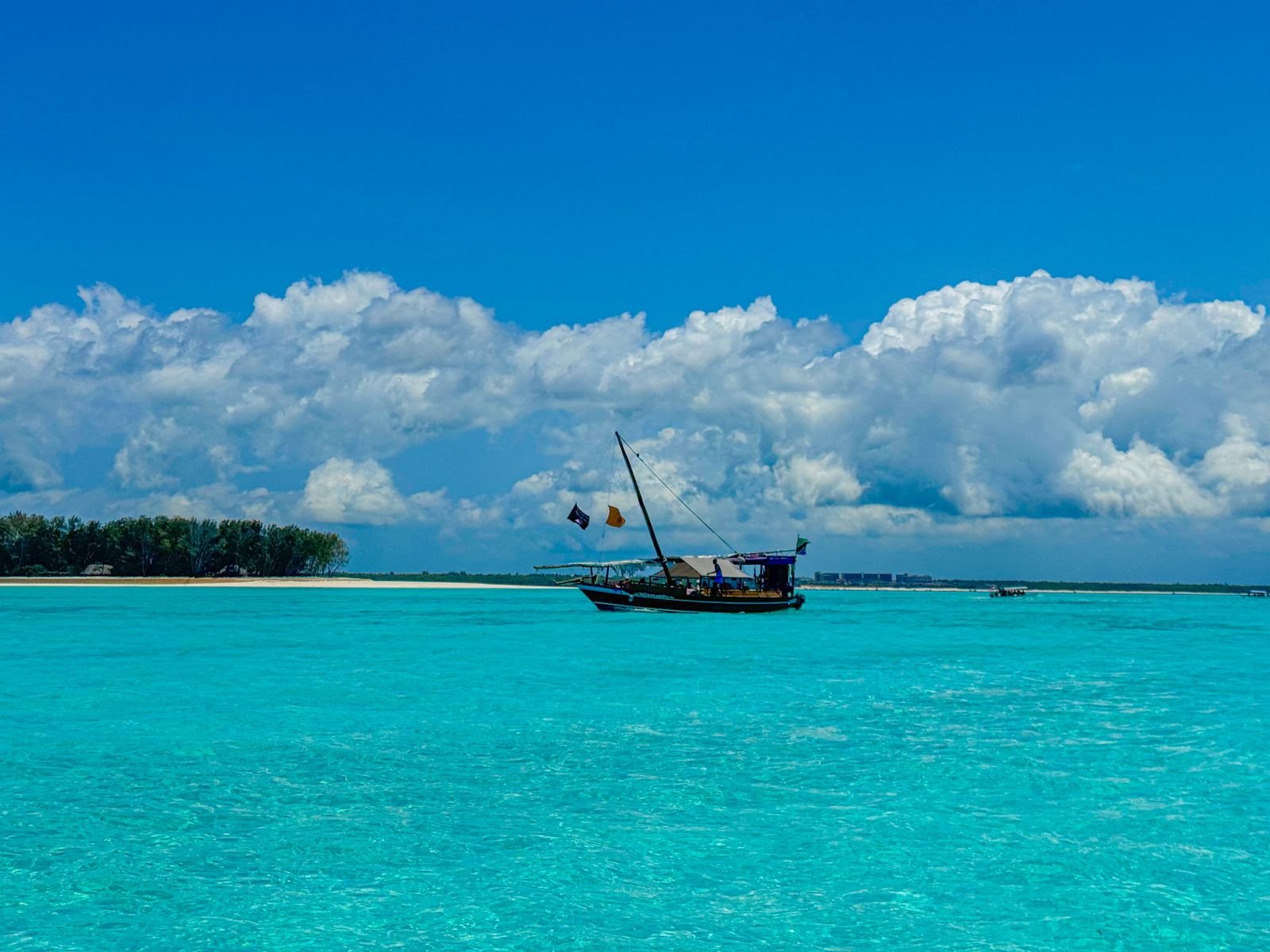 Traditional dhow sailing beside a white-sand Zanzibar beach